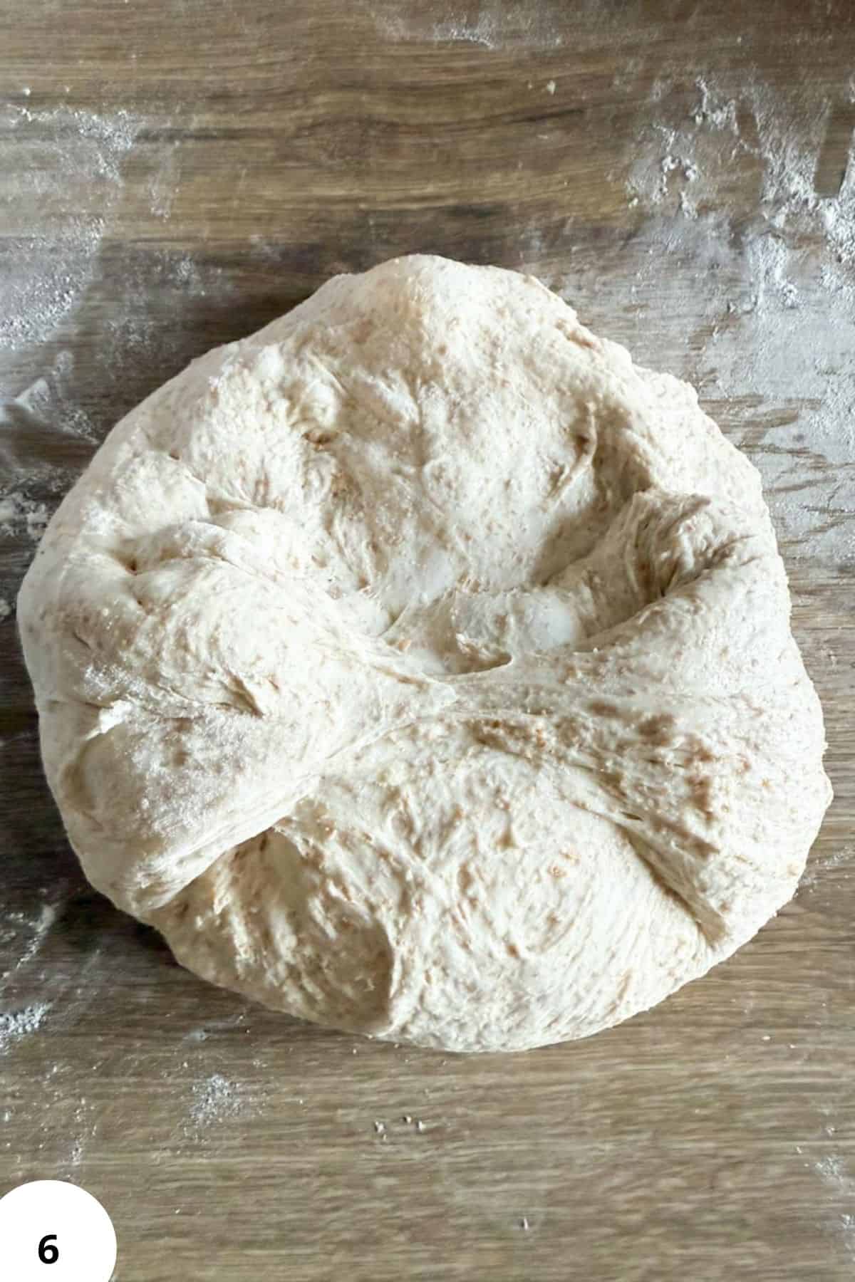 Close-up of soft bread dough on a floured wooden surface.