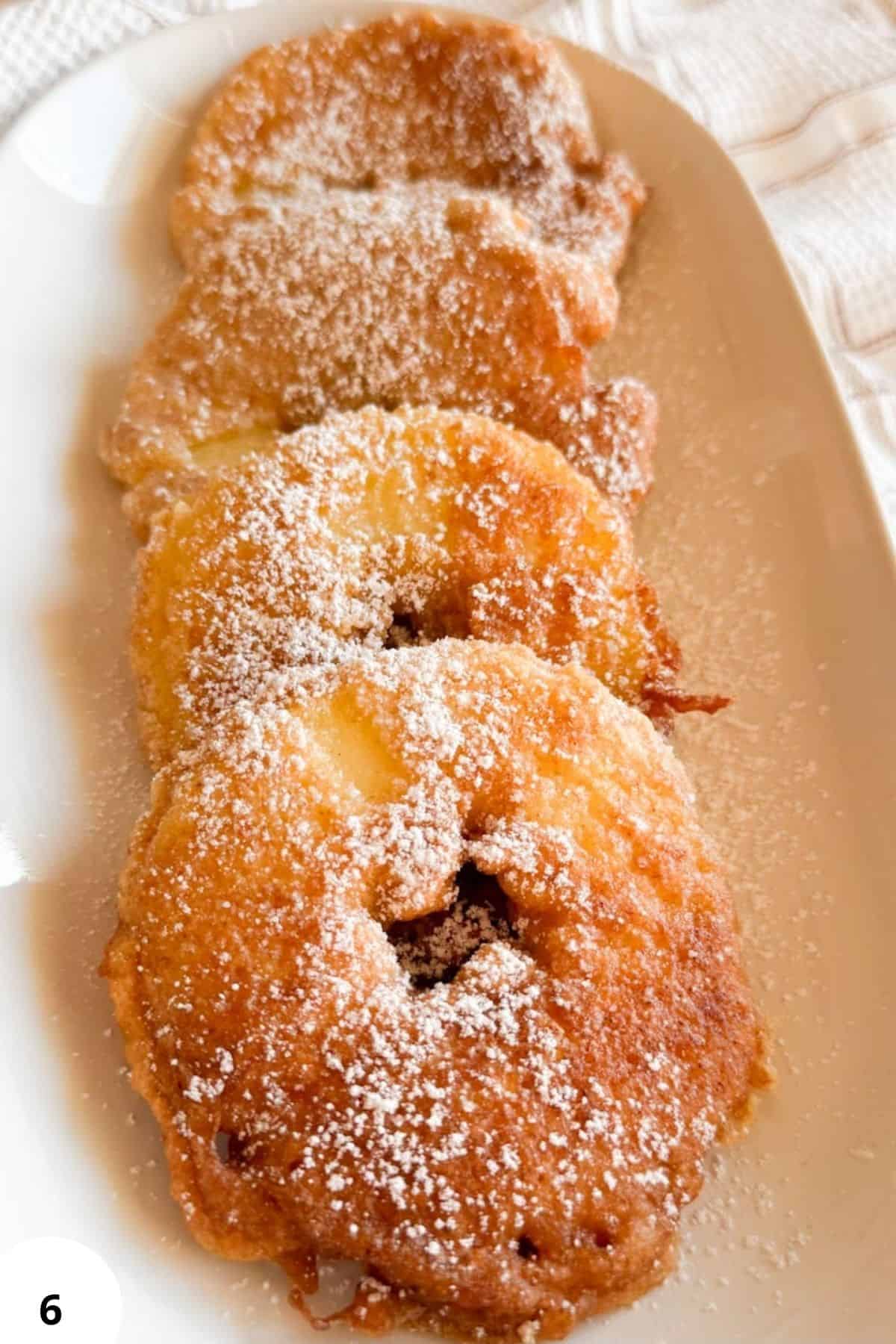 Golden fried apple fritters sprinkled with powdered sugar, perfect for breakfast or dessert.