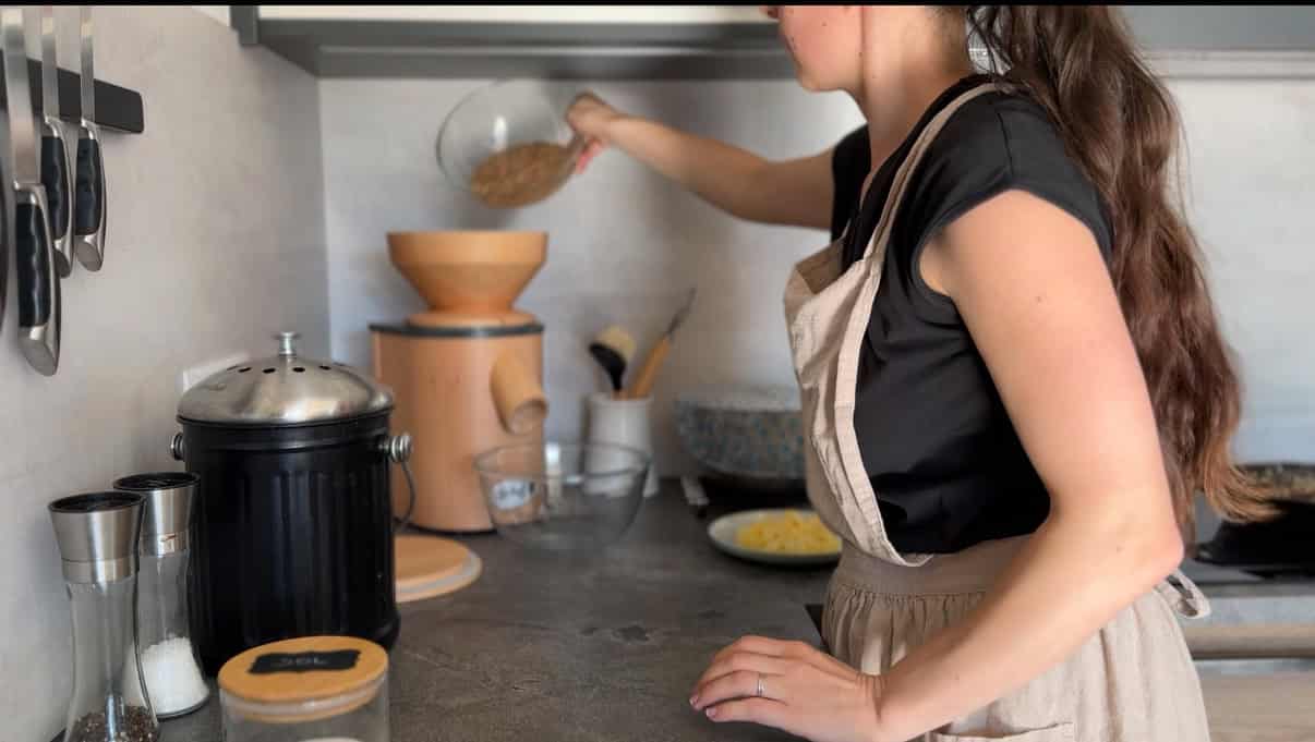 Person pouring grains into a flour mill for fresh milled recipes.