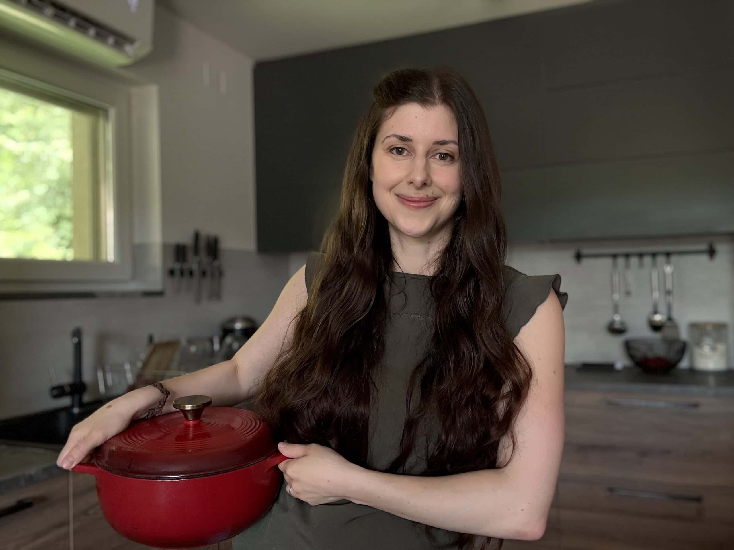 Woman chef holding red cast iron pot in a modern kitchen for healthy, fresh meal preparation.