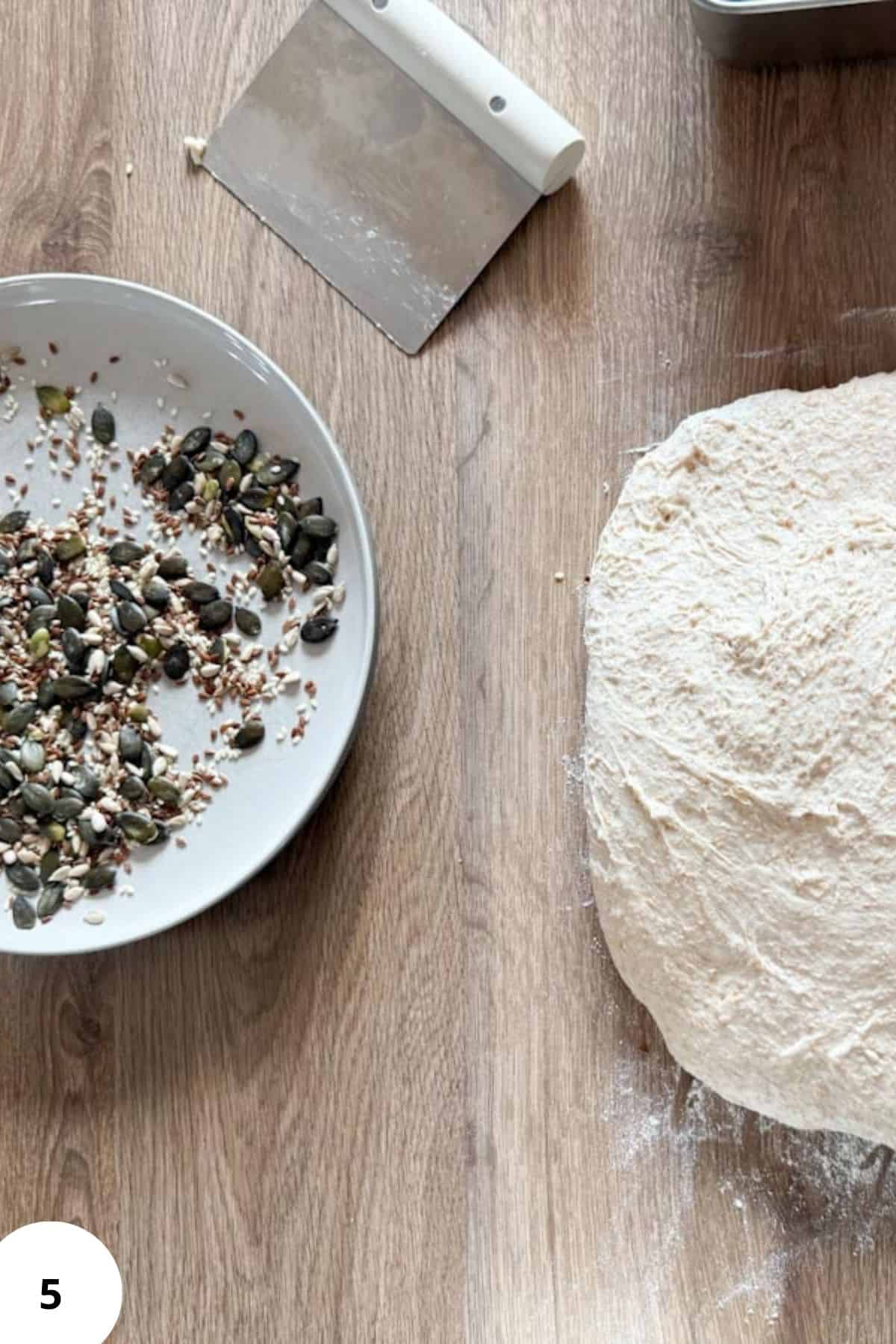 Close-up of a dough ball and a plate of mixed seeds for bread topping.