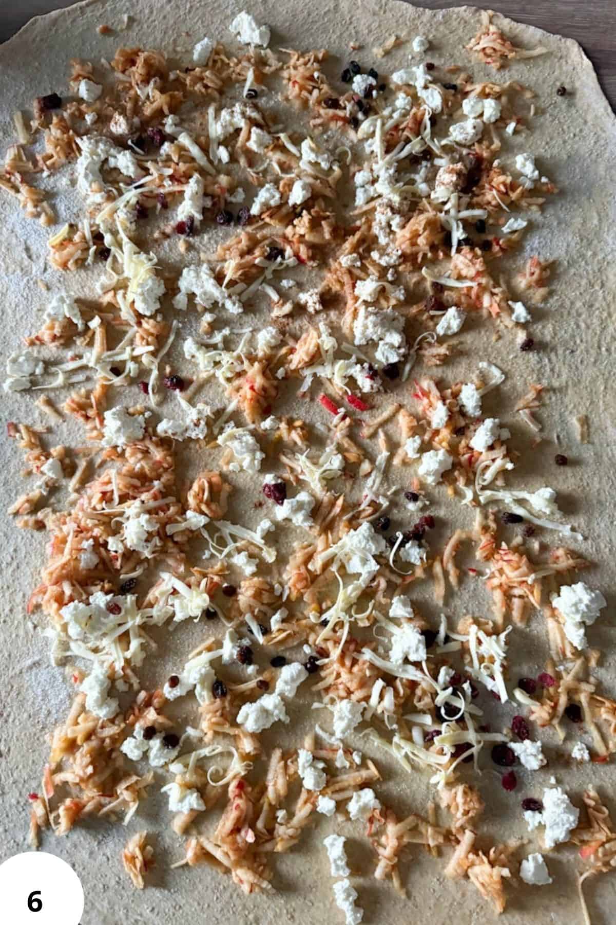 Close-up of uncooked flatbread topped with shredded chicken, cheeses, and herbs.