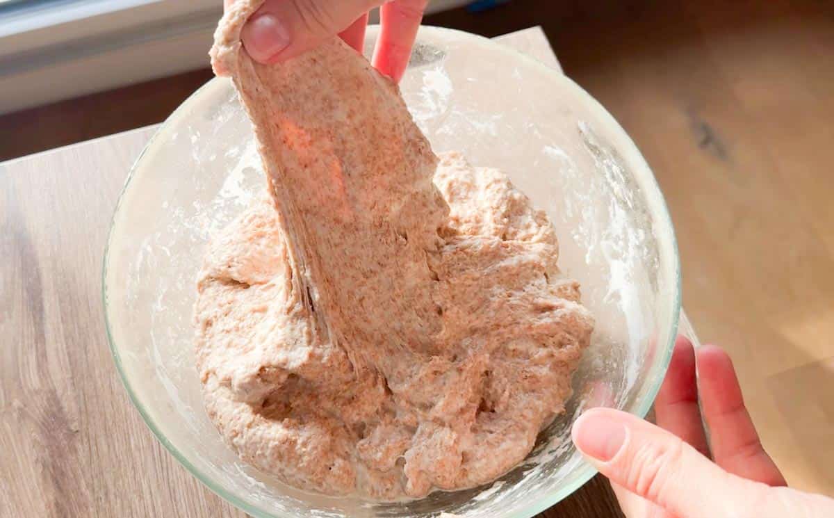A person mixing fresh homemade bread dough in a glass bowl for healthy baking.