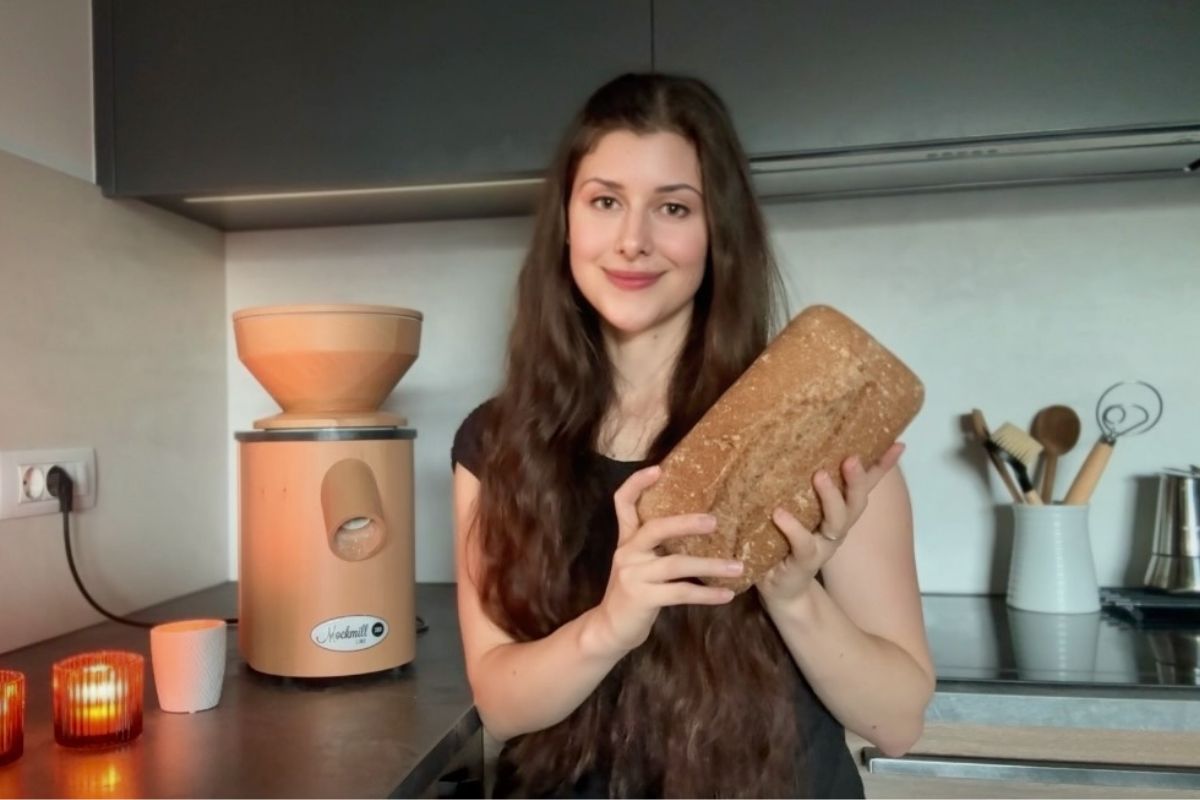 Young woman holding fresh baked bread in a modern kitchen, emphasizing homemade milling and bread recipes.