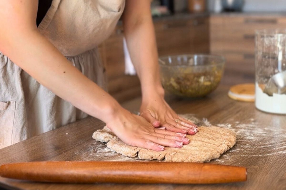 Hand kneading freshly milled whole grain dough on a rustic wooden table.