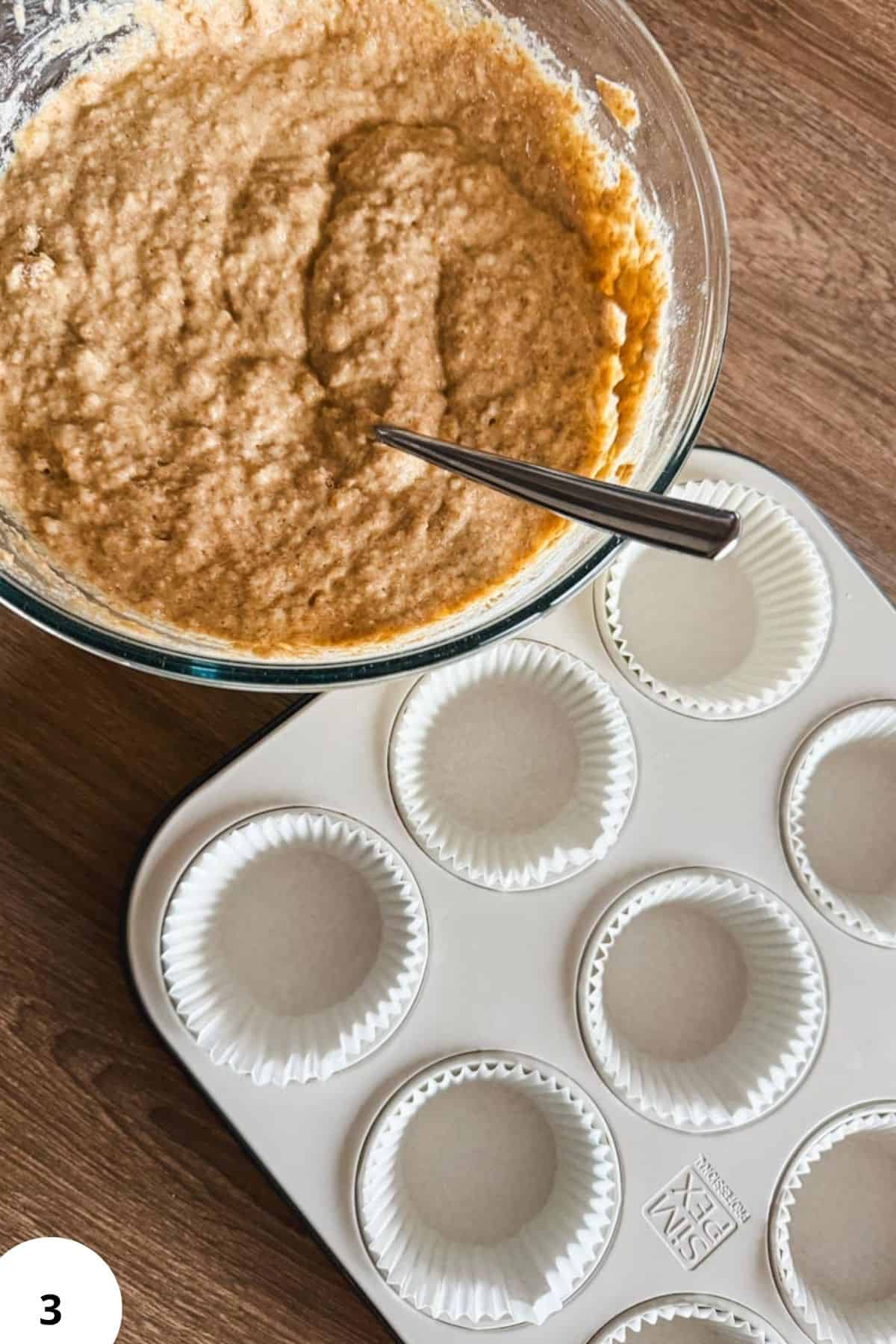 Freshly prepared banana muffin batter in a glass bowl with muffin liners ready for baking.