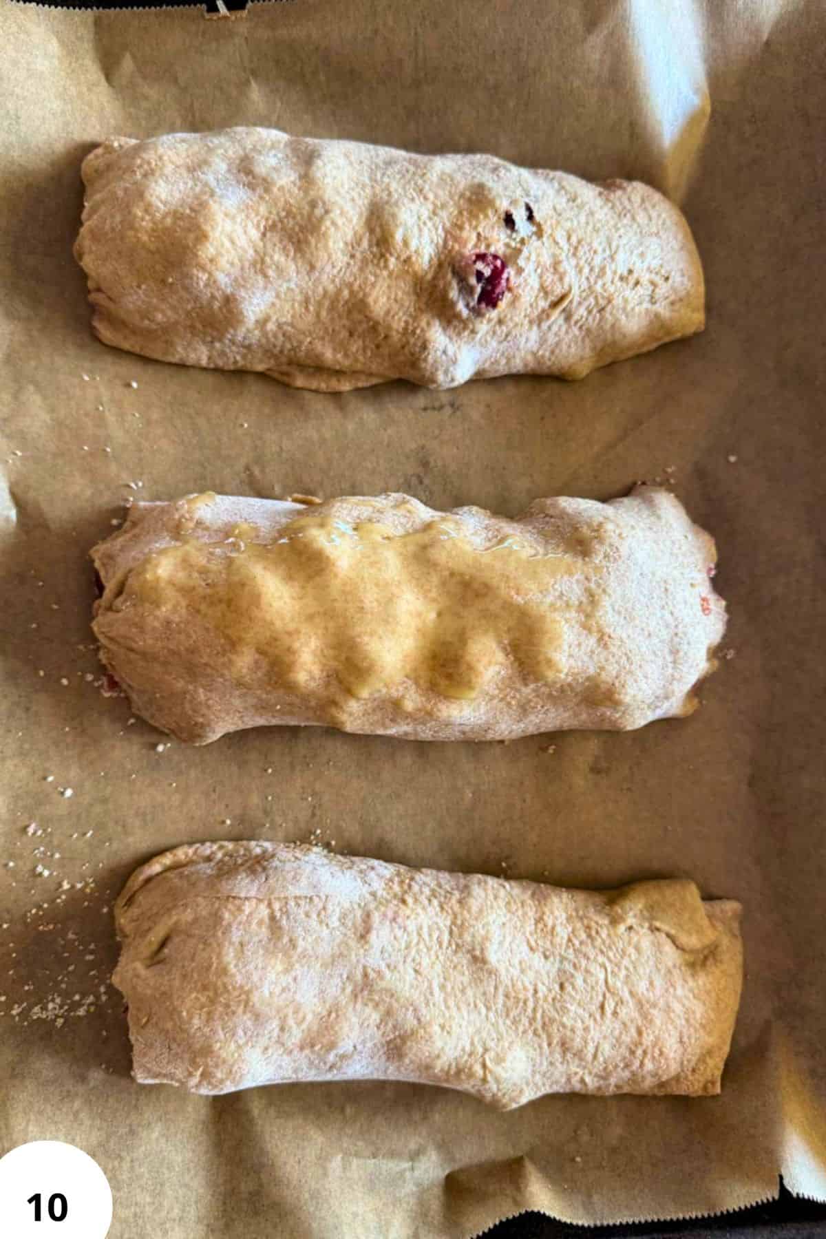 Three freshly baked cherry strudels dusted with powdered sugar on parchment paper.