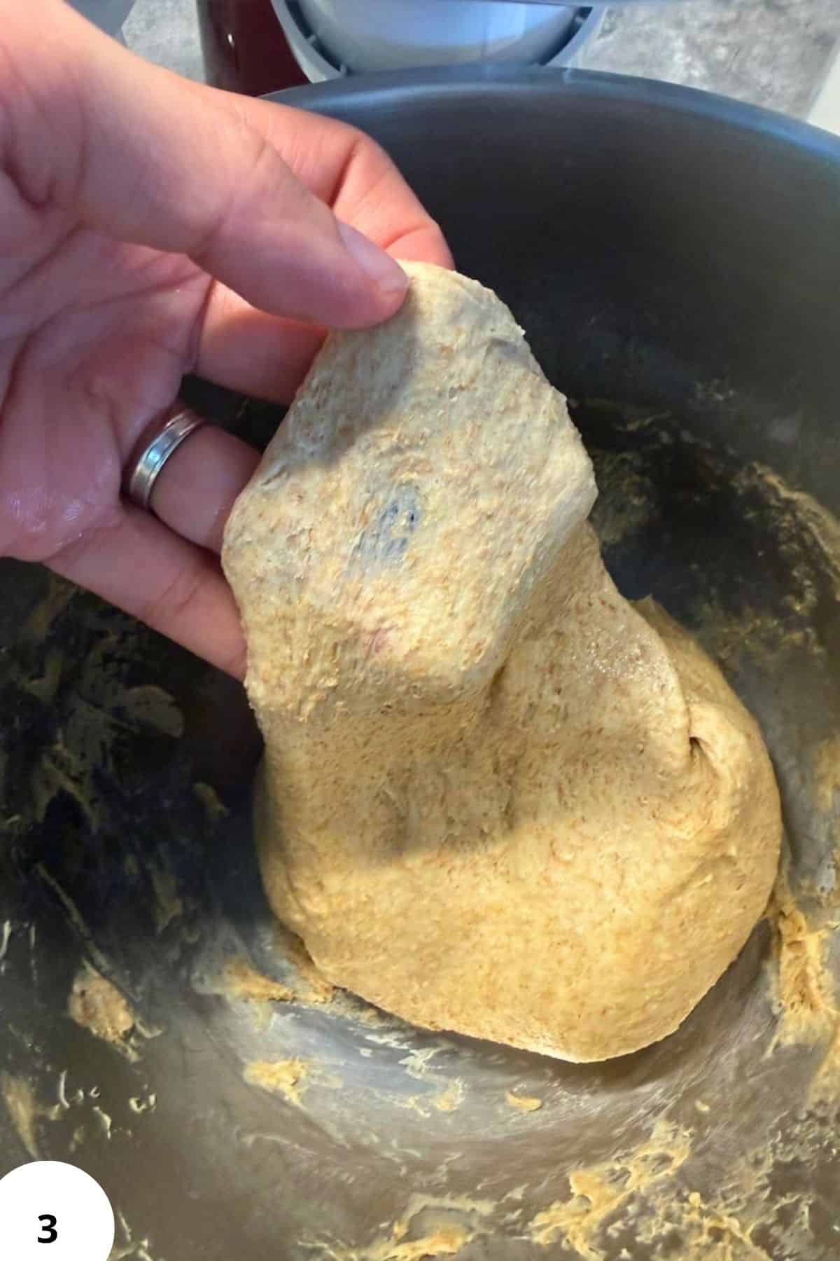 Hand holding dough for cherry strudel in a mixing bowl.