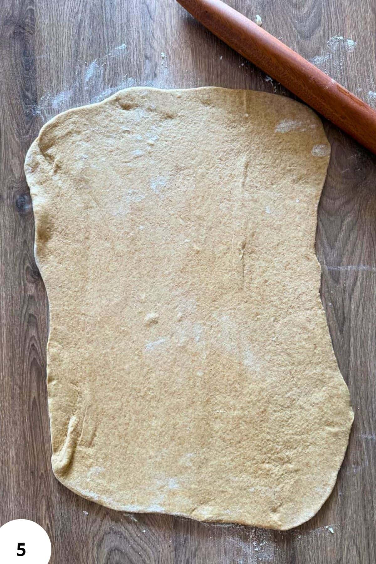 Rolling out dough for cherry strudel on a wooden surface with a rolling pin.
