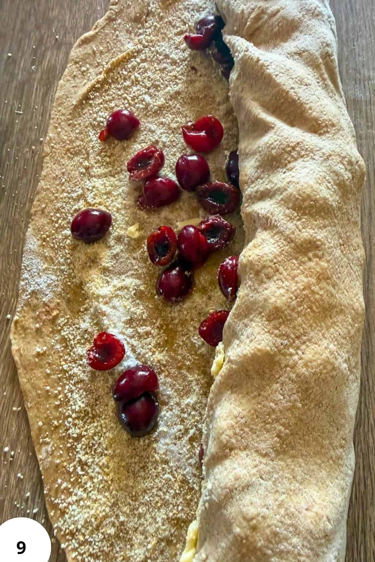 Cherry strudel with fresh cherries and powdered sugar on a wooden surface.