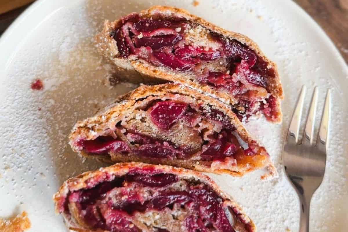 Cherry strudel with flaky crust and cherry filling on a white plate.