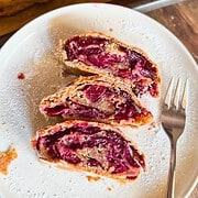 Close-up of cherry strudel slices on a white plate with a fork.