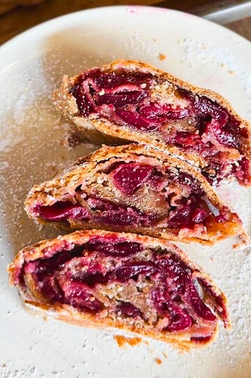 Close-up of cherry strudel slices on a white plate with a fork.