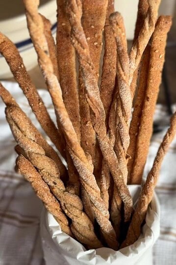 Freshly baked whole wheat breadsticks in a white paper cone.