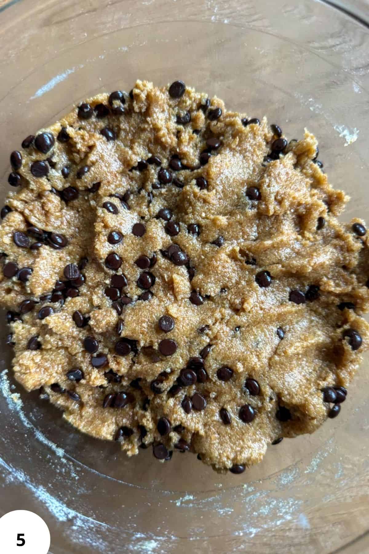 Chocolate chip cookie dough with chocolate chips in a glass bowl.