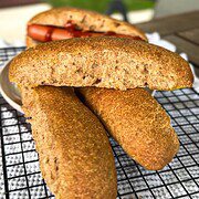 Freshly baked sourdough hot dog buns on a cooling rack with a hot dog in the background.