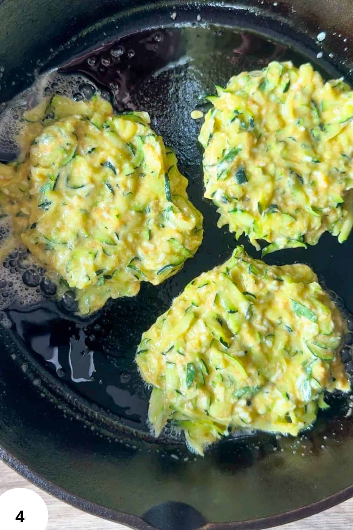 Freshly cooked zucchini fritters in a skillet with herbs and oil.