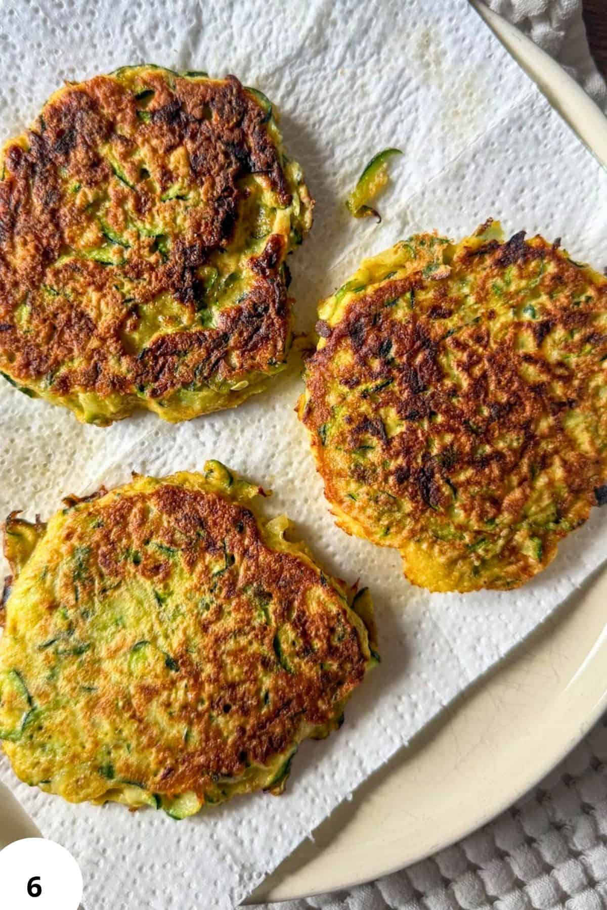 Golden zucchini fritters on a white plate with a crispy exterior.